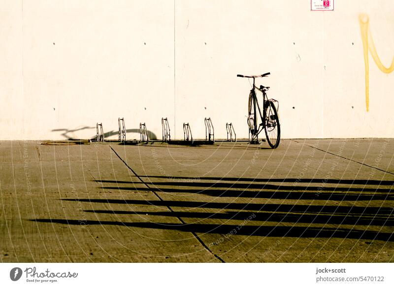 a bicycle and long shadows on the concrete Bicycle rack Parking Means of transport Eco-friendly Concrete wall Concrete floor Parking lot shadow cast turned off