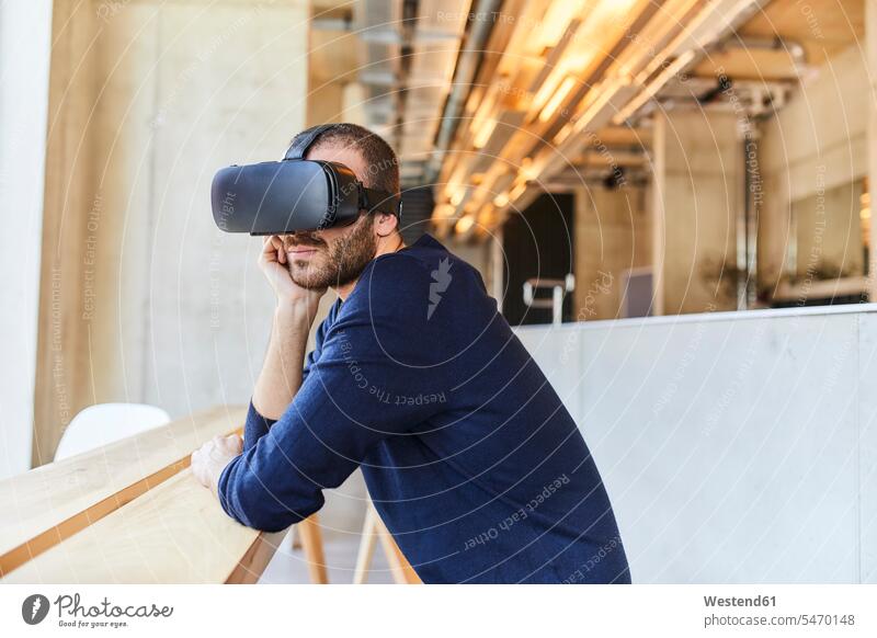 Young man wearing VR glasses in modern office leaning rested on 3D three dimensional Three-Dimensional Shape 3-d offices office room office rooms