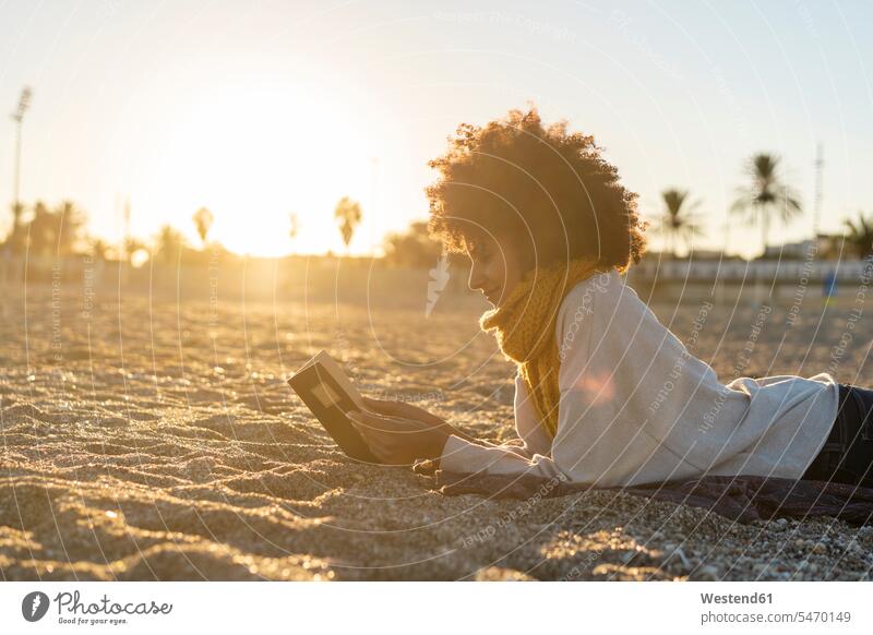 Woman lying in the sand, relaxing on the beach, reading a book sandy relaxation relaxed mid adult women mid adult woman mid-adult women mid-adult woman beaches