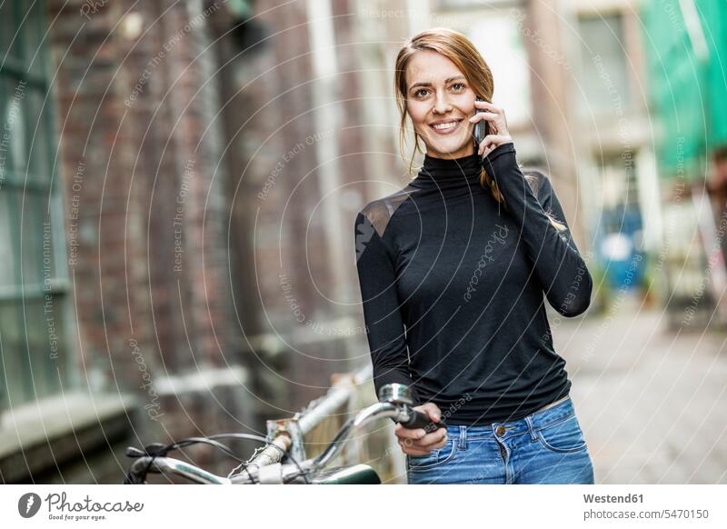 Portrait of smiling woman with bicycle on the phone females women portrait portraits smile bikes bicycles call telephoning On The Telephone calling Adults