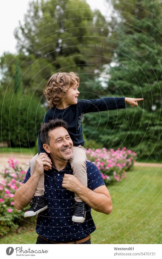 Happy father carrying son on shoulders in park parks happiness happy fathers daddy dads papa sons manchild manchildren parents family families people persons
