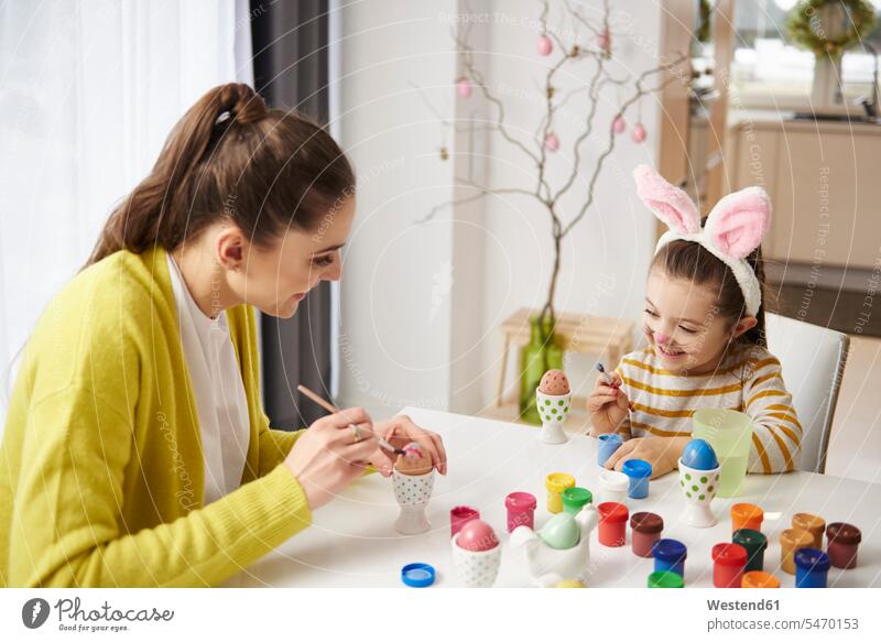 Happy mother and daughter with bunny ears sitting at table painting Easter eggs Rabbit Ears Bunny Ear Bunny Ears costume rabbit ears girl females girls