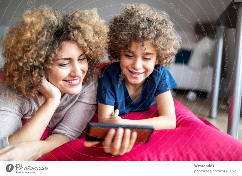 Mother and son watching a video on smartphone, lying on big pillow human human being human beings humans person persons caucasian appearance caucasian ethnicity