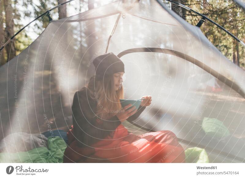 Young woman sitting in tent, eating breakfast in the forest caps hat hats human human being human beings humans person persons caucasian appearance