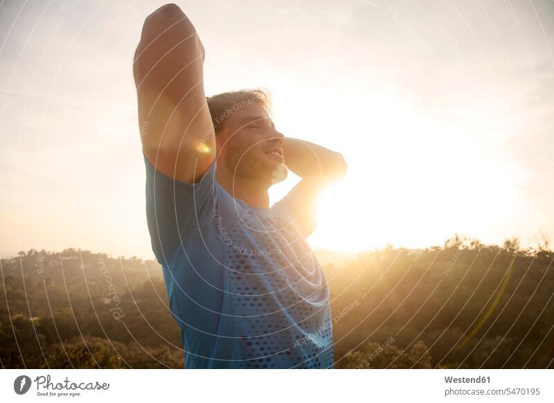Man stretching arms while standing against sky color image colour image outdoors location shots outdoor shot outdoor shots sunset sunsets sundown atmosphere
