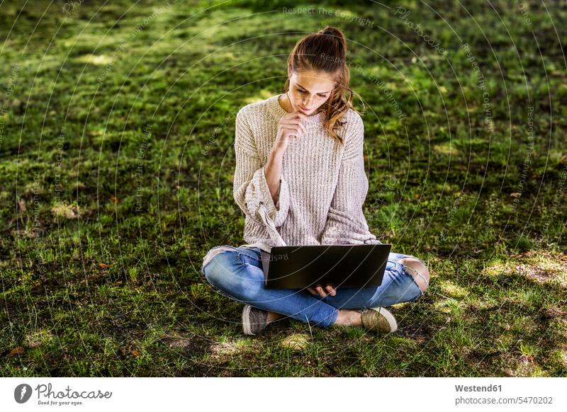 Pensive woman sitting on a meadow using laptop Laptop Computers laptops notebook pensive thoughtful Reflective contemplative females women meadows use Seated