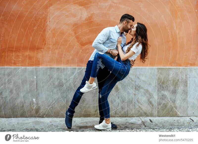 Affectionate couple in love kissing in front of a wall outdoors Love loving twosomes partnership couples kisses walls positive Emotion Feeling Feelings