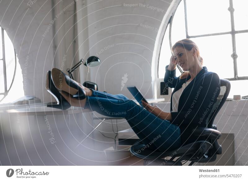 Businesswoman using tablet with feet on desk in office businesswoman businesswomen business woman business women offices office room office rooms smiling smile
