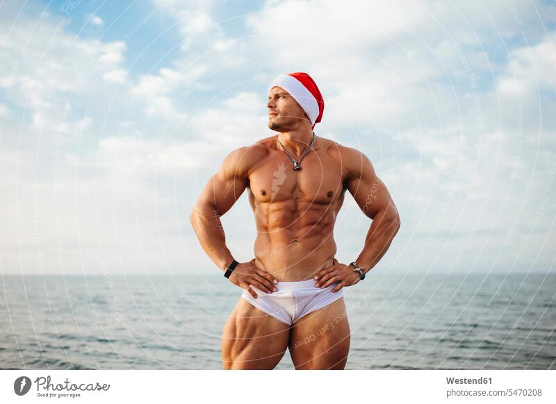 Shirtless macho man wearing Santa hat standing against sea color image colour image Spain leisure activity leisure activities free time leisure time outdoors