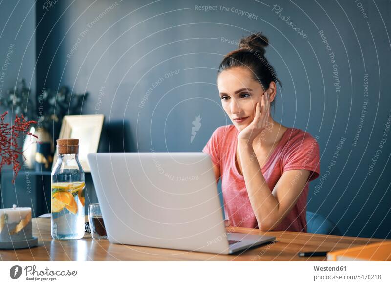 Female entrepreneur using laptop on desk against wall in home office color image colour image casual clothing casual wear leisure wear casual clothes