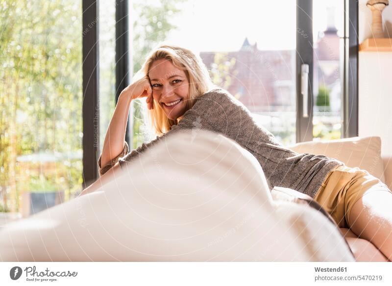 Portrait of happy mature woman relaxing on couch at home relaxation happiness females women portrait portraits settee sofa sofas couches settees Adults