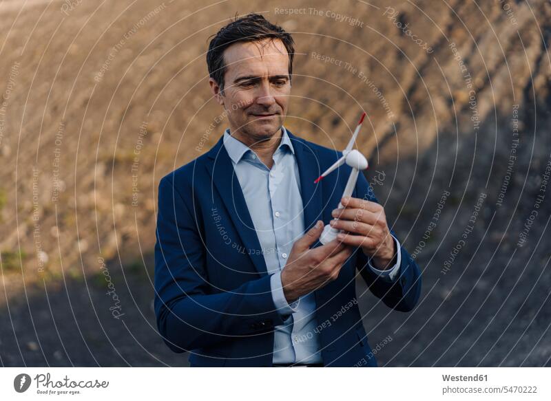 Mature businessman on a disused mine tip holding wind turbine model human human being human beings humans person persons caucasian appearance