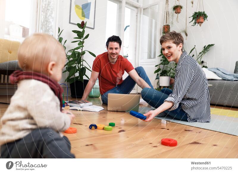 Happy family sitting on ground, playinhg with their little daughter home at home playing Seated happiness happy Sitting On The Floor Sitting On Floor toy toys