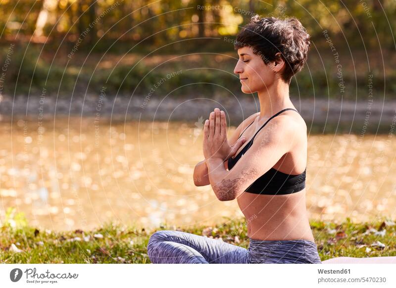 Mid adult woman at riverside practicing yoga, meditation Yogini Yoginis forest woods forests meditating meditations training Sport Training sitting Seated