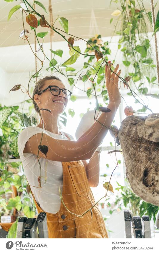 Smiling young woman caring for plants in a small shop Occupation Work job jobs profession professional occupation windows Eye Glasses Eyeglasses specs