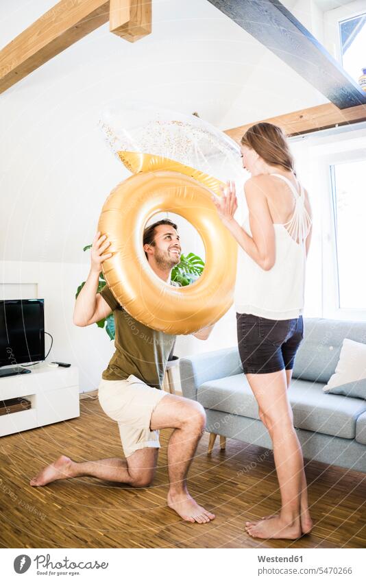 Smiling man looking at girlfriend through large inflatble ring at home eyeing rings happiness happy inflatable blow-up smiling smile couple twosomes partnership