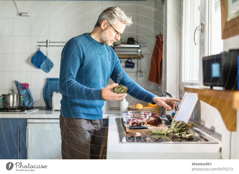 Mature man preparing salad in his kitchen using digital tablet human human being human beings humans person persons caucasian appearance caucasian ethnicity