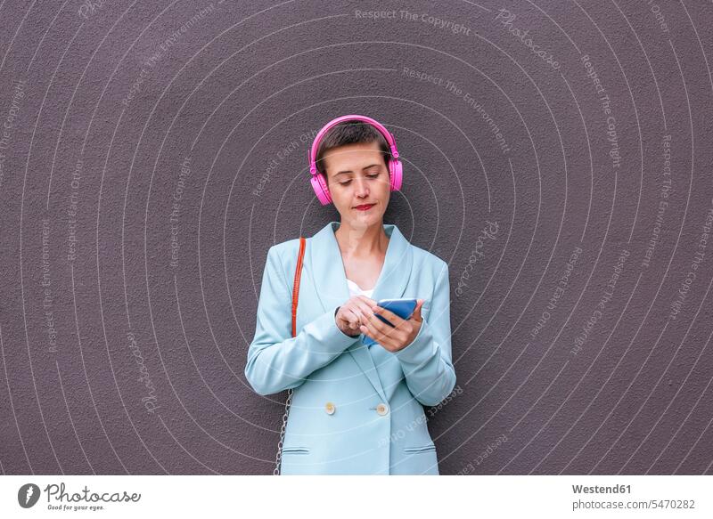 Woman dressed in jacket listening to music with her mobile phone suit coat suit jacket Smartphone iPhone Smartphones headphones headset woman females women