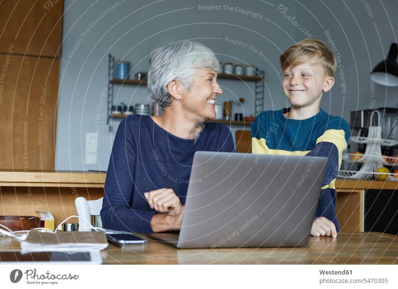 Smiling grandson standing next to grandmother working on laptop at home color image colour image indoors indoor shot indoor shots interior interior view