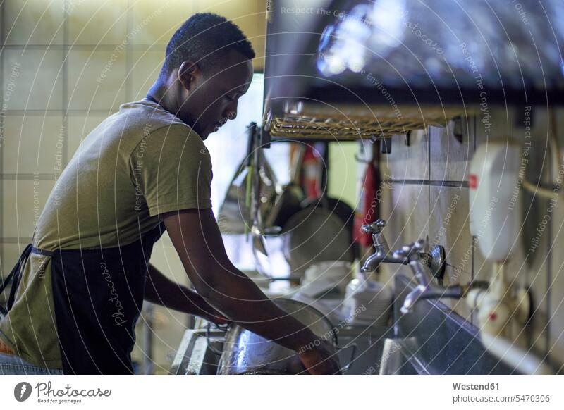 Young man washing dishes in restaurant kitchen, South Africa Occupation Work job jobs profession professional occupation Crockery Tableware Cooking Pots At Work