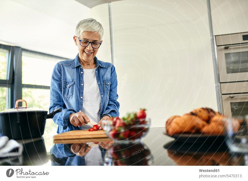 Senior woman standing in kitchen, chopping strawberries human human being human beings humans person persons caucasian appearance caucasian ethnicity european
