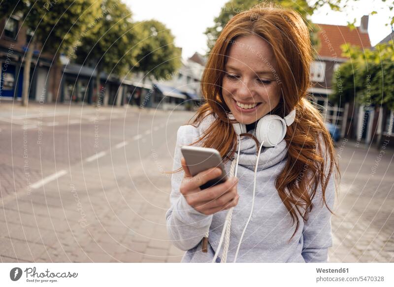 Redheaded woman using headphones and smartphone in the city headset urban urbanity females women Smartphone iPhone Smartphones on the phone call telephoning