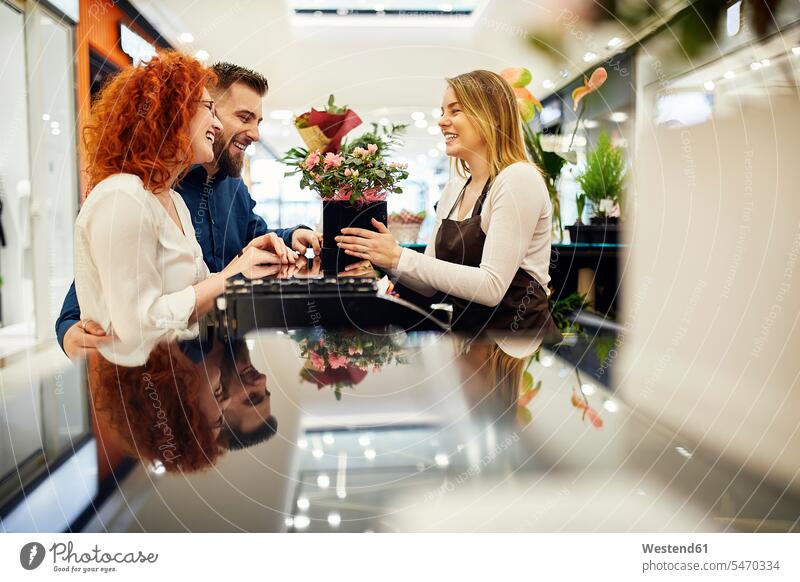 Happy couple and shop assistant with potted plant at counter in flower shop customer clientele clients customers shop assistants potted plants pot  plants