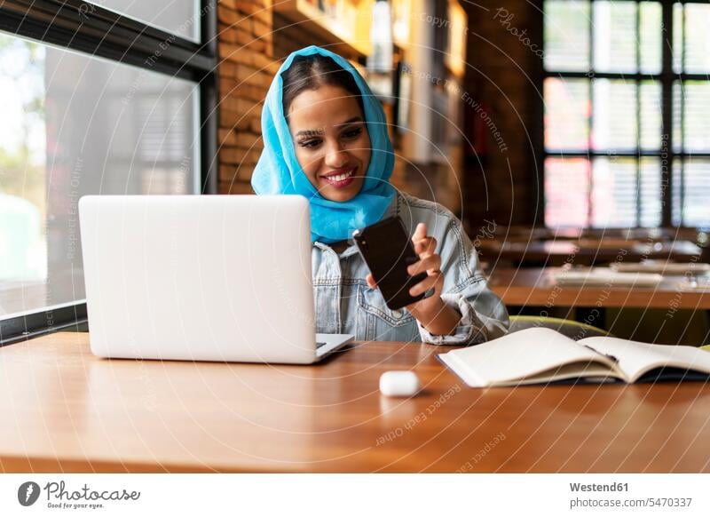 Businesswoman wearing turquoise hijab in a cafe and working, using laptop and looking on smartphone Occupation Work job jobs profession professional occupation