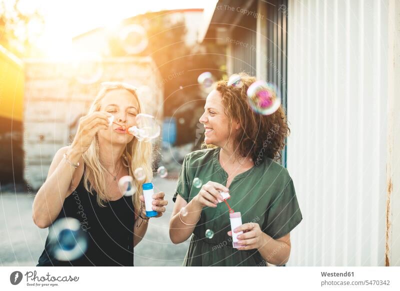 Two happy women blowing soap bubbles outdoors woman females female friends Fun having fun funny happiness Adults grown-ups grownups adult people persons