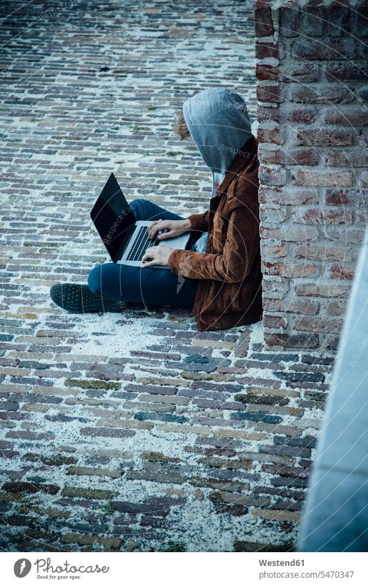 Teenager using laptop and sitting on a stone floor in the city criminals hoods computers Laptop Computer Laptop Computers laptops notebook Seated free time