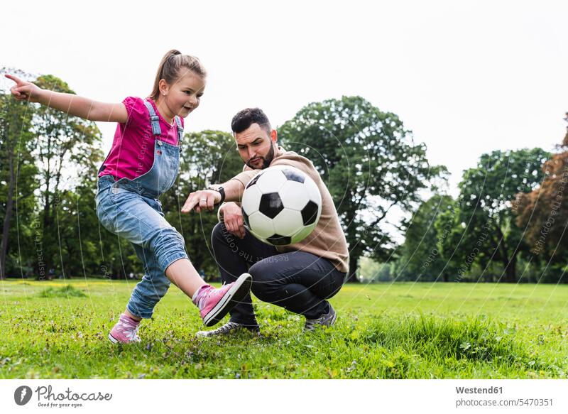 Father playing football with daughter in a park daughters happiness happy active parks soccer father fathers daddy dads papa child children family families