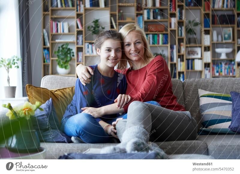Mother and adolescent daughter sitting on couch with arms around settee sofa sofas couches settees understanding childhood toothy smile big smile open smile