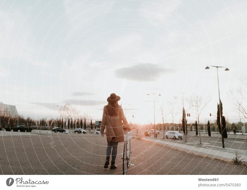 Young hipster woman going with a bicycle during sunset hat hats Coat Coats pushing Sustainable transport females women bikes bicycles walking Mobility mobile