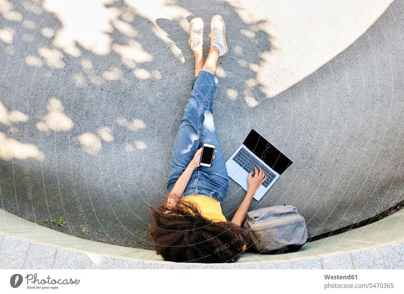 Student with mobile phone using laptop while sitting on footpath color image colour image outdoors location shots outdoor shot outdoor shots day daylight shot