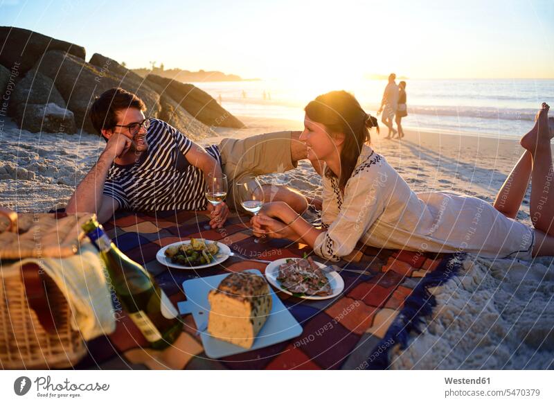 Happy couple having a picnic on the beach at sunset sunsets sundown beaches twosomes partnership couples Picnic picnicking happiness happy atmosphere