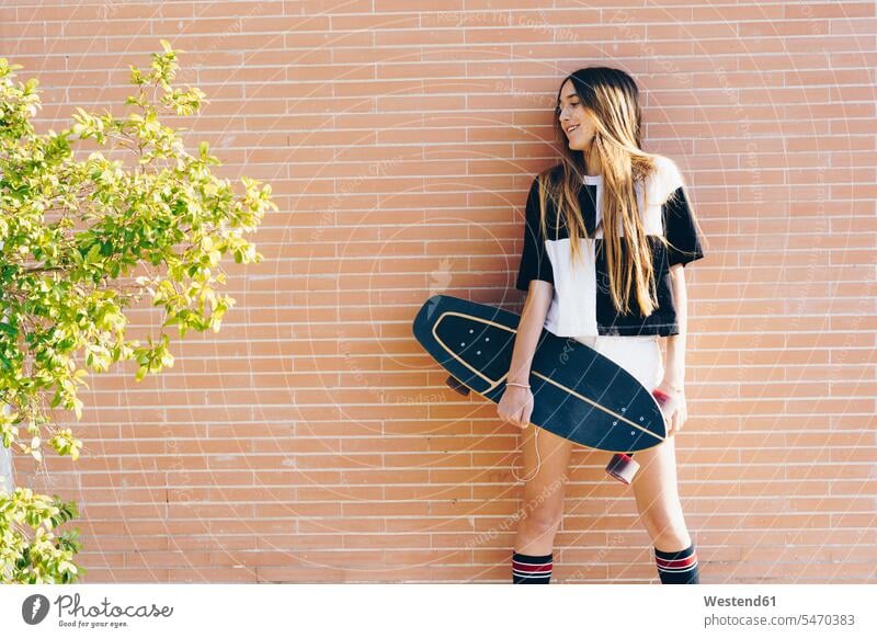 Spain, teenage girl holding skateboard at a brick wall smiling smile brick walls Skate Board skateboards happiness happy Teenage Girls female teenagers Teenager