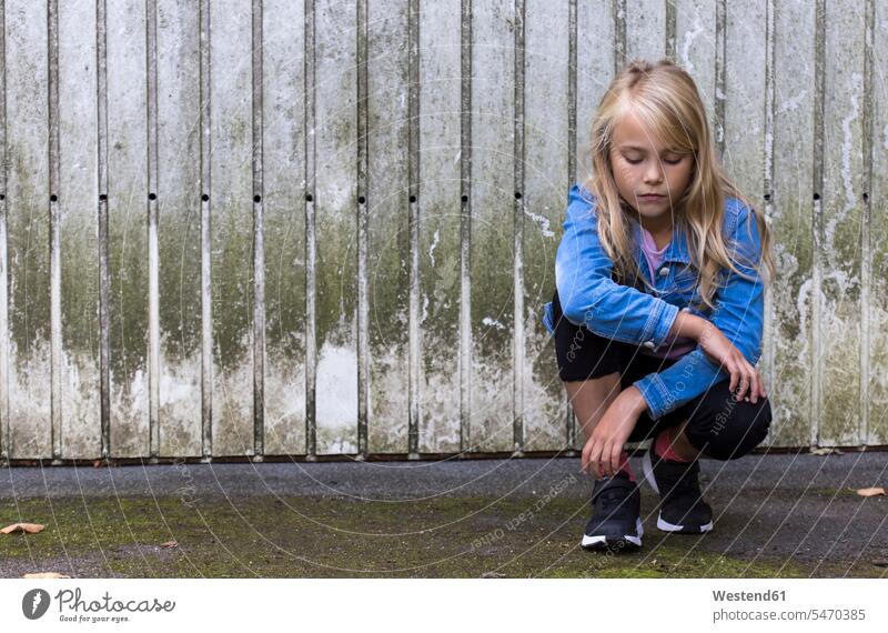 Portrait of serious blond girl crouching in front of wooden wall earnest Seriousness austere wooden walls cowering portrait portraits females girls blond hair