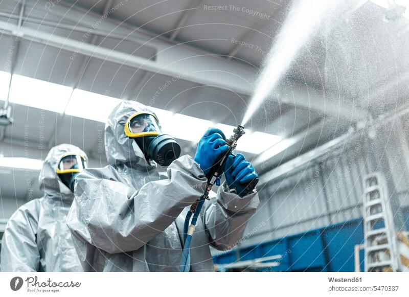 Low angle view of sanitation workers spraying chemical from hose in warehouse color image colour image Corona Virus Coronavirus disease Covid-19 COVID19