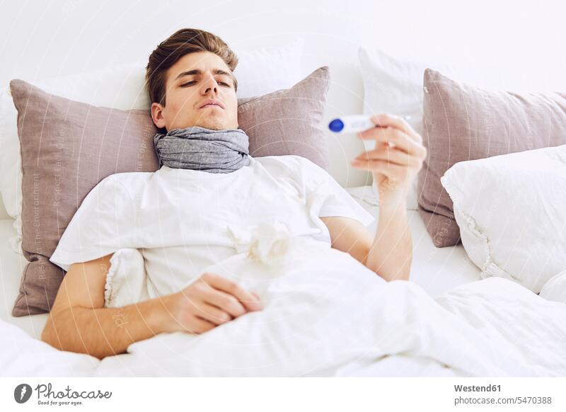 Sick man examining temperature with thermometer while resting on bed at home color image colour image Germany indoors indoor shot indoor shots interior
