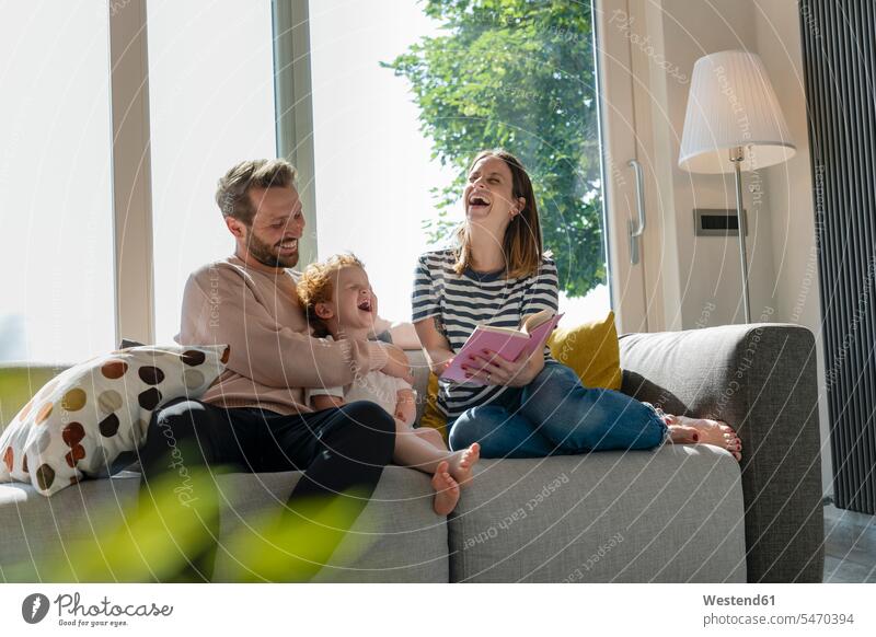 Cheerful family enjoying reading story book while sitting on sofa at home color image colour image indoors indoor shot indoor shots interior interior view