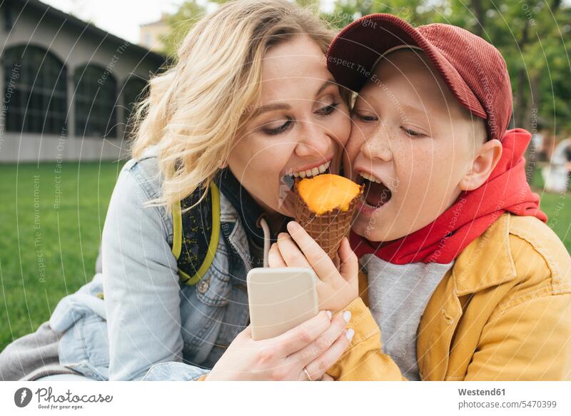 Mother and son eating ice cream together telecommunication phones telephone telephones cell phone cell phones Cellphone mobile mobile phones mobiles hold Seated