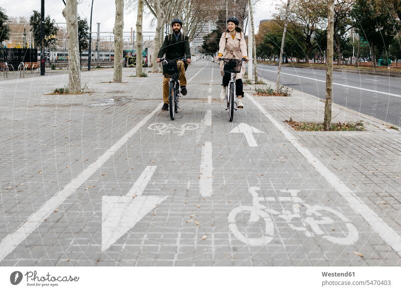 Couple riding e-bikes in the city on bicycle lane town cities towns Bike Lane cycle path E-Bike Electric bicycle Electric Bike couple twosomes partnership