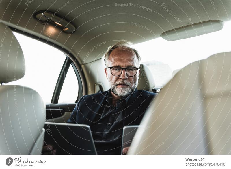 Mature businessman sitting on backseat in car, using digital tablet automobile Auto cars motorcars Automobiles back seat Smartphone iPhone Smartphones digitizer