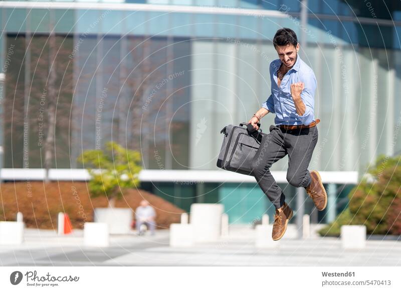 Young excited businessman holding briefcase while jumping outdoors color image colour image location shots outdoor shot outdoor shots day daylight shot