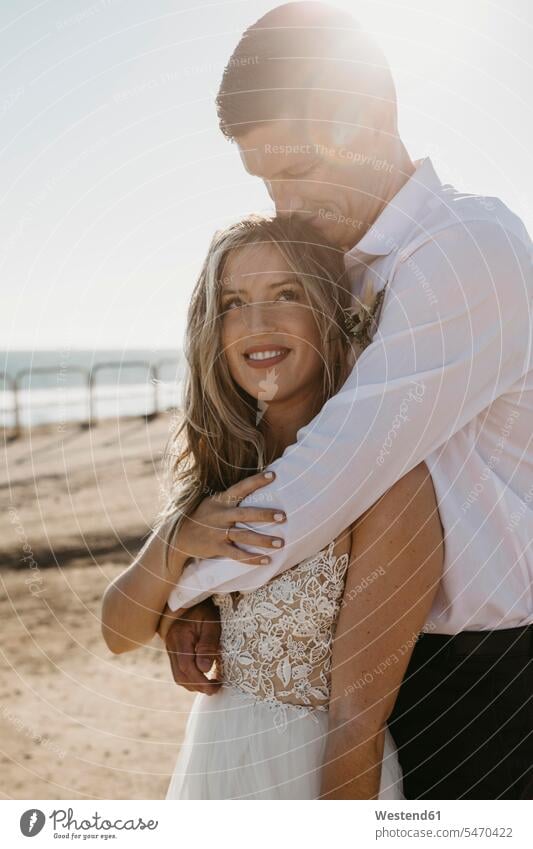 Affectionate bride and groom hugging on the beach at sunset Celebration Event Celebrations Ceremonies Ceremony Festivities Festivity getting married Marriage