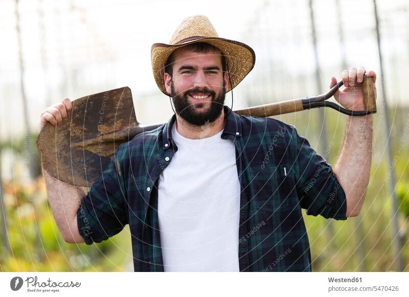 Portrait of smiling young man holding a shovel in a greenhouse Occupation Work job jobs profession professional occupation blue collar blue collar worker
