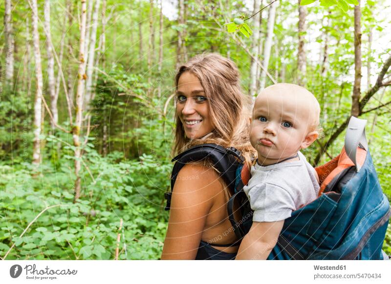 Portrait of smiling mother hiking in the woods with baby boy in backpack hike portrait portraits mommy mothers ma mummy mama rucksacks backpacks back-packs