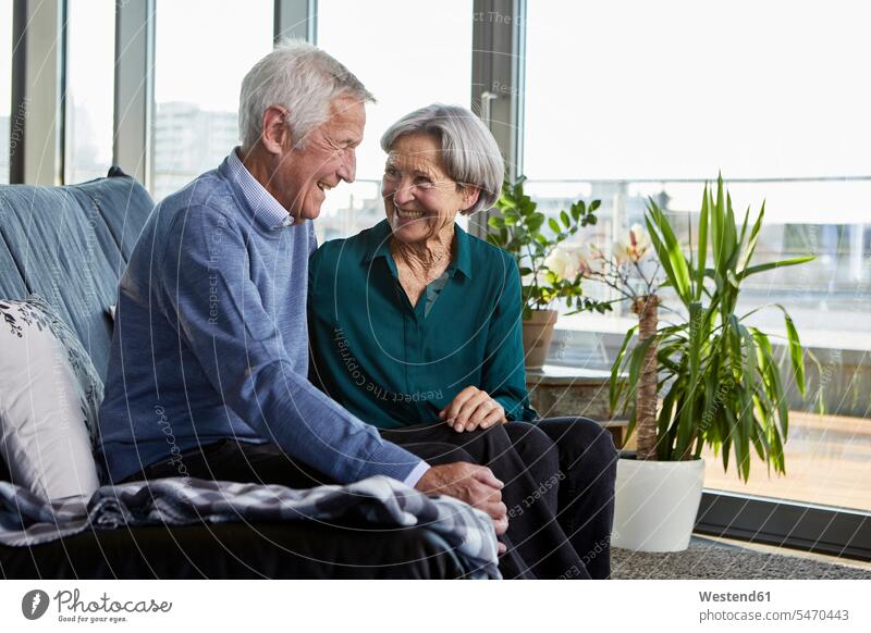 Laughing senior couple sitting together on couch settee sofa sofas couches settees Seated laughing Laughter elder couples senior couples twosomes partnership