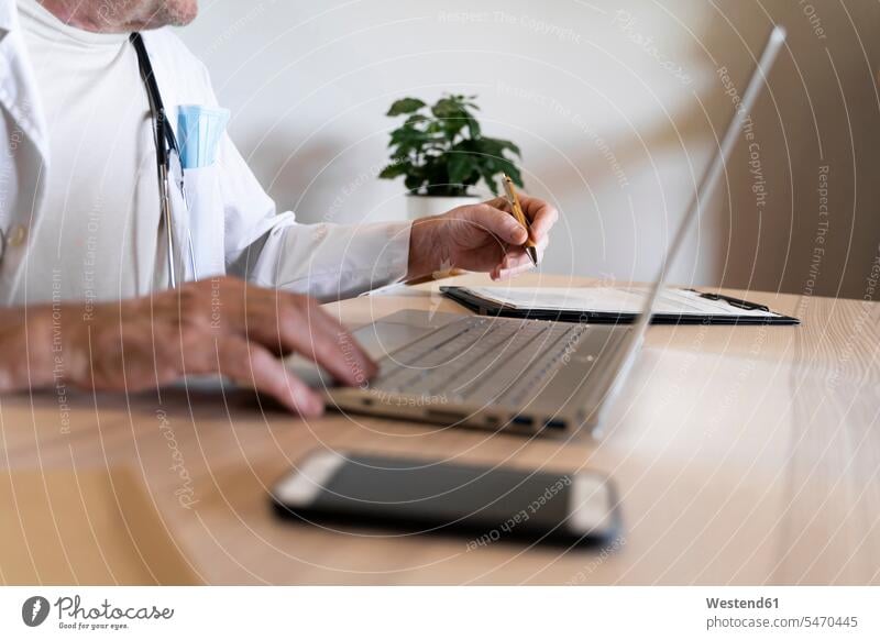 Doctor using laptop while sitting at desk in clinic color image colour image indoors indoor shot indoor shots interior interior view Interiors day daylight shot