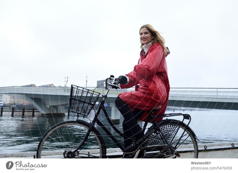 Denmark, Copenhagen, happy woman riding bicycle at the waterfront in rainy weather bikes bicycles females women happiness Adults grown-ups grownups adult people